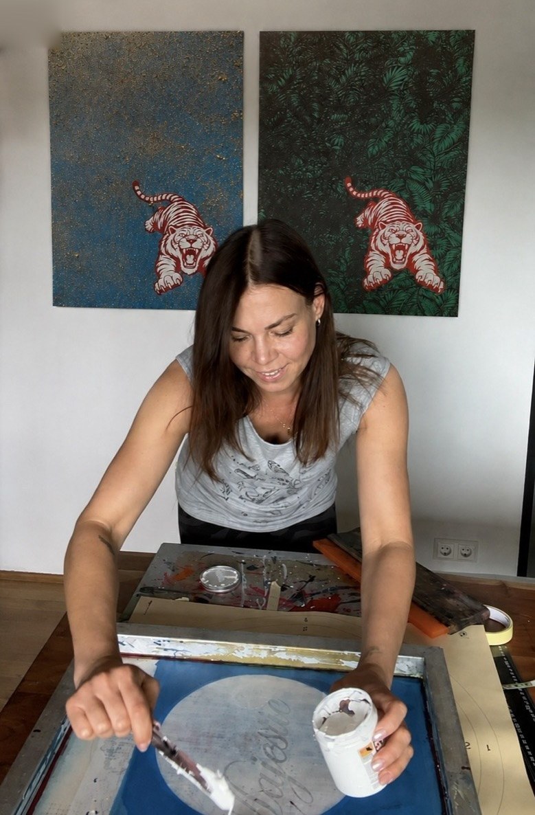 Britta Streng an der Siebdruckpresse im Atelier, im Hintergrund zwei Tigerdrucke auf Leinwand